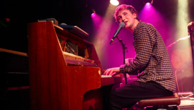 Dove Ellis achter zijn piano kijkt het publiek in