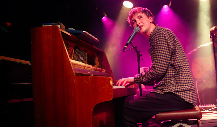 Dove Ellis achter zijn piano kijkt het publiek in