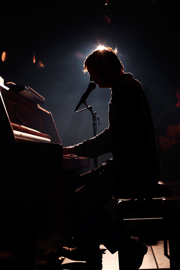 Dove Ellis zittend achter piano met licht achter zijn hoofd in de tolhuistuin