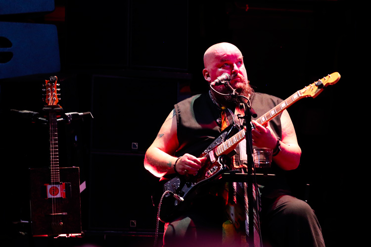 Alain Johannes speelt zittend gitaar in de band Drink the Sea bij hun optreden in Paradiso